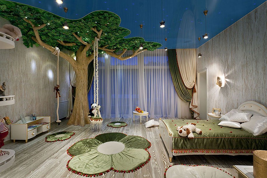 A whimsical children's bedroom with a large artificial tree, a rope swing, green leaf-shaped rugs, and a bed with a stuffed dog on it