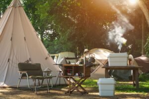 Camping site with teepee tent, camping gear, and cooking area set up under the trees with sunlight filtering through